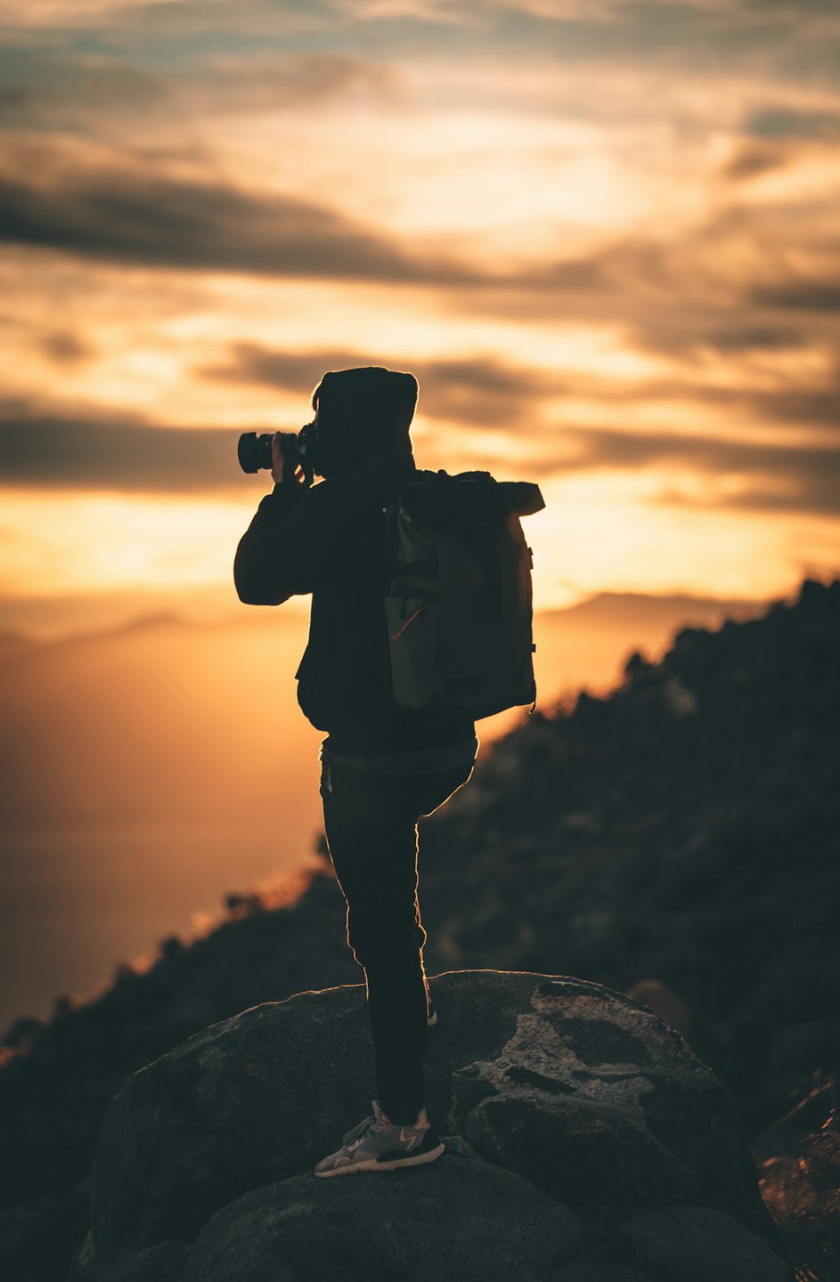 Photographer silhouetted against a vibrant sunset over mountains.